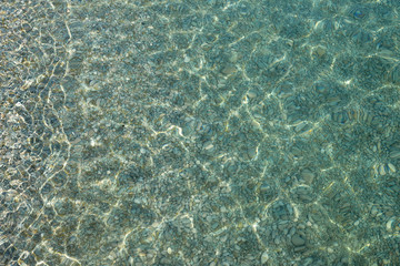 Shimmering sun glares on pebble seabed under water as background