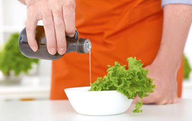 Chef pouring olive oil over fresh salad in restaurant kitchen closeup.