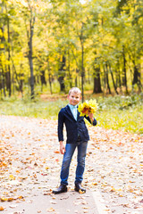 Handsome little boy in sunny autumn park with maple leaves