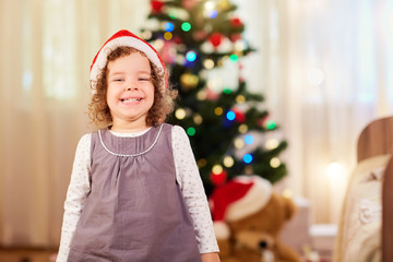 Little girl in Christmas hat Santa Claus smiling in the room. Ha
