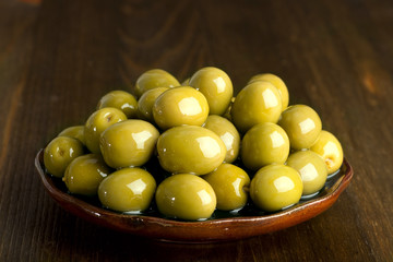 green olives in oil stacked on a ceramic plate