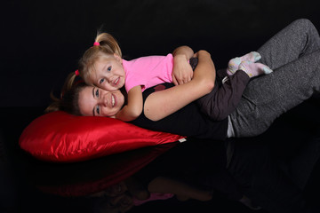 Matka z córką leżą przytulone na czerwonej poduszce.. - obrazy, fototapety, plakaty