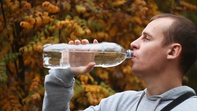 Young man drinking water after workout at the gym. Autumn composition
