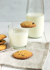 Homemade cookies with chocolate pieces and milk on a white table.