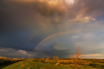 Ominous stormy sky at evening, and beautiful after rain rainbow, in remote rural field
