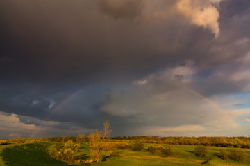 Ominous stormy sky at evening, and beautiful after rain rainbow, in remote rural field