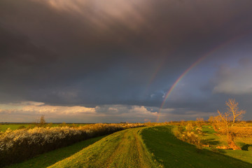 Ominous stormy sky at evening, and beautiful after rain rainbow, in remote rural field
