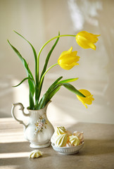 Spring flowers still life . Fresh yellow tulips bouquet in vase. Meringue cookies.