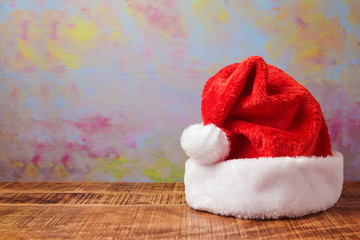 Obraz na płótnie Canvas Christmas santa hat on wooden table over artistic background