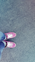 Fototapeta premium Pink sneakers shoes walking on concrete top view with sunlight. Leather shoes and feet on concrete top view background. Selfie image.
