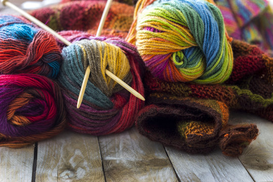 Colorful skeins of wool with knitting needles and sweater on wooden background