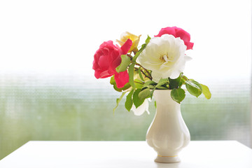 Beautiful bouquet of cream and pink rose flowers in vase with green bokeh background.