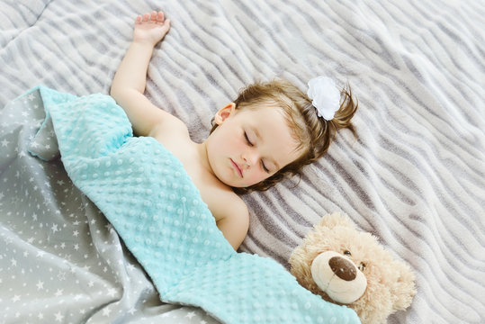 Close-up portrait of a beautiful sleeping baby girl. Cute infant kid with teddy bear. Child portrait in pastel tones.Top view image.
