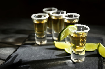 Gold tequila shots with lime and salt on wooden table