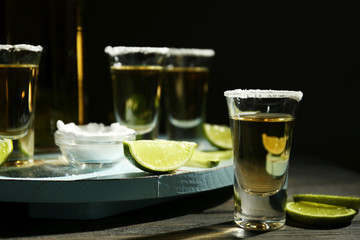 Gold tequila shot with lime and salt on wooden table