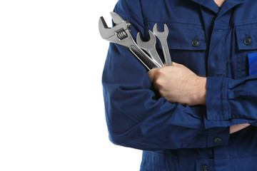 Mechanic in uniform with crossed arms and wrenches standing on white background