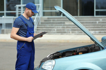 Mechanic with a clipboard and pen standing near open car hood