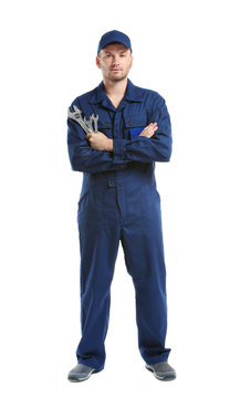 Young mechanic in uniform with crossed arms and wrenches standing, isolated on white