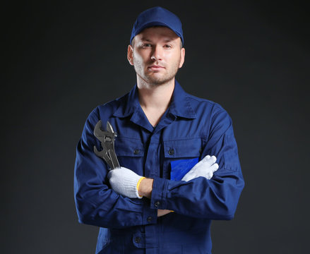 Young Mechanic In Uniform  And Gloves With A Wrench Standing On A Black Background