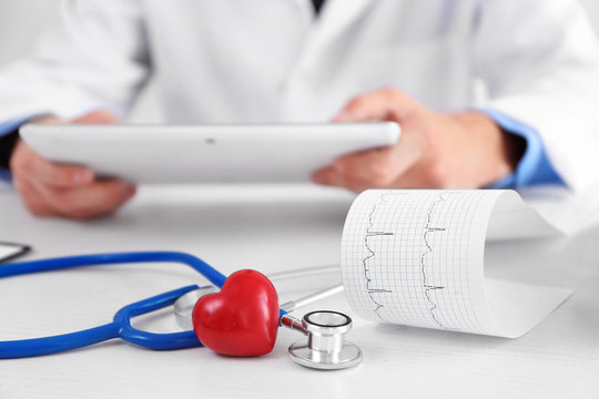 Cardiogram, stethoscope and red heart on doctor table, close up view