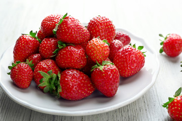 Plate with juicy strawberries on white wooden background