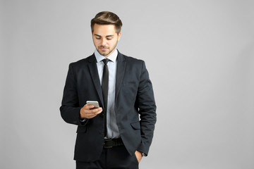 Obraz na płótnie Canvas Handsome young businessman with phone on gray background