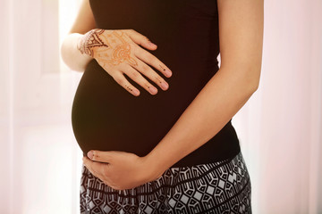 Young pregnant woman with henna tattoo on hand on light background