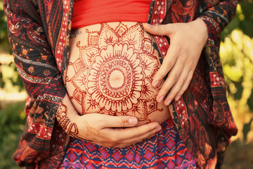 Young pregnant woman with henna tattoo on belly in park