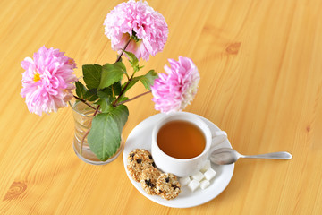 Breakfast still life. Cookies with cup of tea and flowers. Top view.