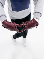 Top view girl wearing skates shows abstract heart symbol by leather gloves on ice. Concept of love to skating, winter sports.