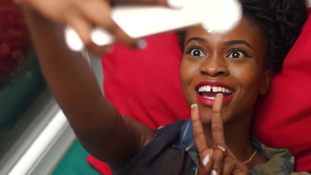 Portrait of beautiful african-american girl making funny selfies with a cell phone