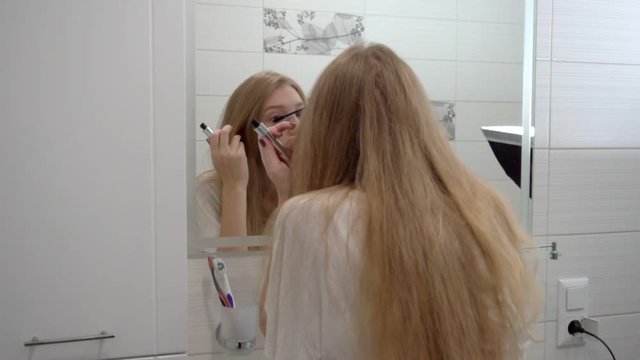 Portrait of woman apply mascara on eyelashes in bathroom mirror at home