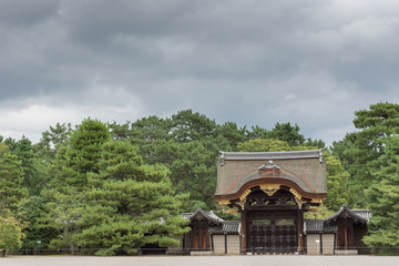 Kyoto, Japan - September 14, 2016: The charming Kenshun-mon gate stands between a row of green trees under heavy skies. Wood carvings and golden trim.
