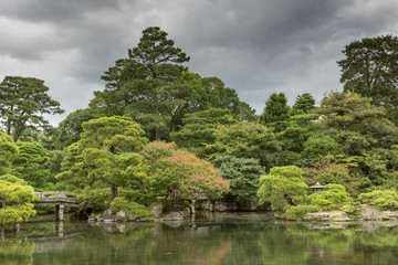 Fototapeta na wymiar Kyoto, Japan - September 14, 2016: Part of the Japanese garden at the imperial palace showing bridge, pond, trees and flowers under heavy sky.