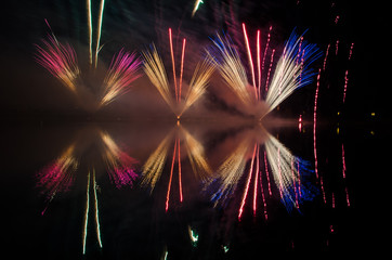 Fireworks display at night with reflections on water