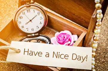 Have a nice day on paper tag with vintage pocket watch and rose in wooden box on wooden background.
