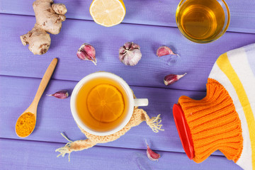 Hot water bottle, cup of tea and ingredients for preparation warming beverage