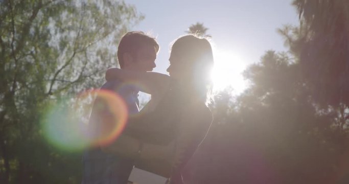Attractive dating couple dance in park in Los Angeles.  Medium shot, recorded hand-held in slow motion with low sun and strong lens flare.