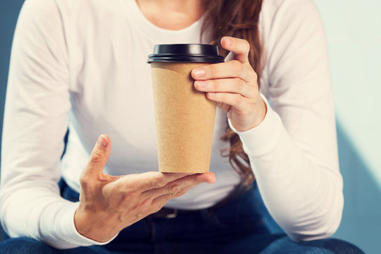 Young woman drinking coffee from disposable brown paper cup