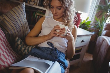 Beautiful woman reading book while having coffee in living room