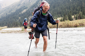 Hiker crossing river at mountains.