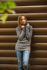 Beautiful girl in a sweater with long hair and red lips on the background of wooden logs