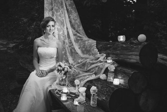 A black and white picture of a happy bride sitting on decorated logs