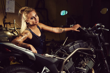 Naklejka na ściany i meble Blond woman mechanic in a motorcycle workshop