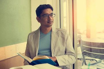 indian male reading book at cafe