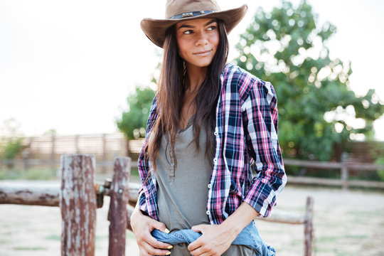 Beautiful young woman cowgirl in hat standing on ranch