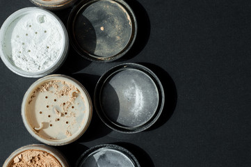 Background with mineral make-up powder of white and beige colors on black surface