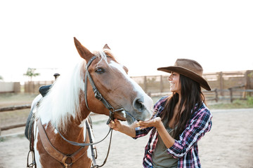 Cheerful woman cowgirl playing with horse in countryside