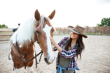 Smiling woman cowgirl enjoying taking care of horse in village