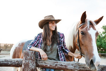 Smilng woman cowgirl standing with her horse on ranch